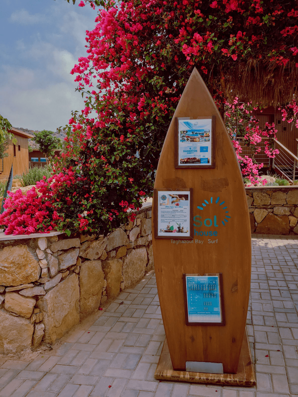 sol house taghazout bay resort surf board display with an activities and events calendar surrounded by pink flowers, stone, and bungalows sol house taghazout bay resort surf board display with an activities and events calendar surrounded by pink flowers, stone, and bungalows