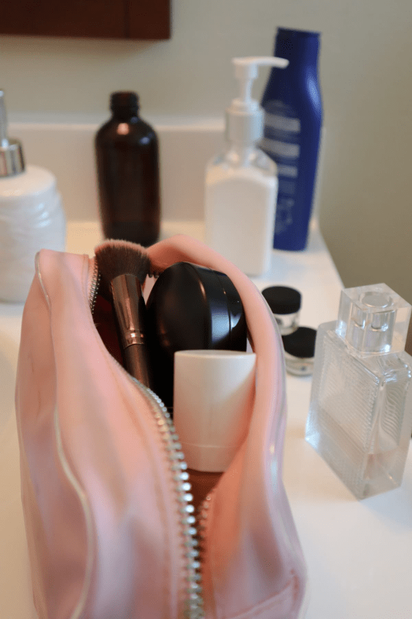 Pink makeup bag with foundation, foundation makeup brush, glass jars, perfume bottle, lotion and hand soap on bathroom counter Pink makeup bag with foundation, foundation makeup brush, glass jars, perfume bottle, lotion and hand soap on bathroom counter