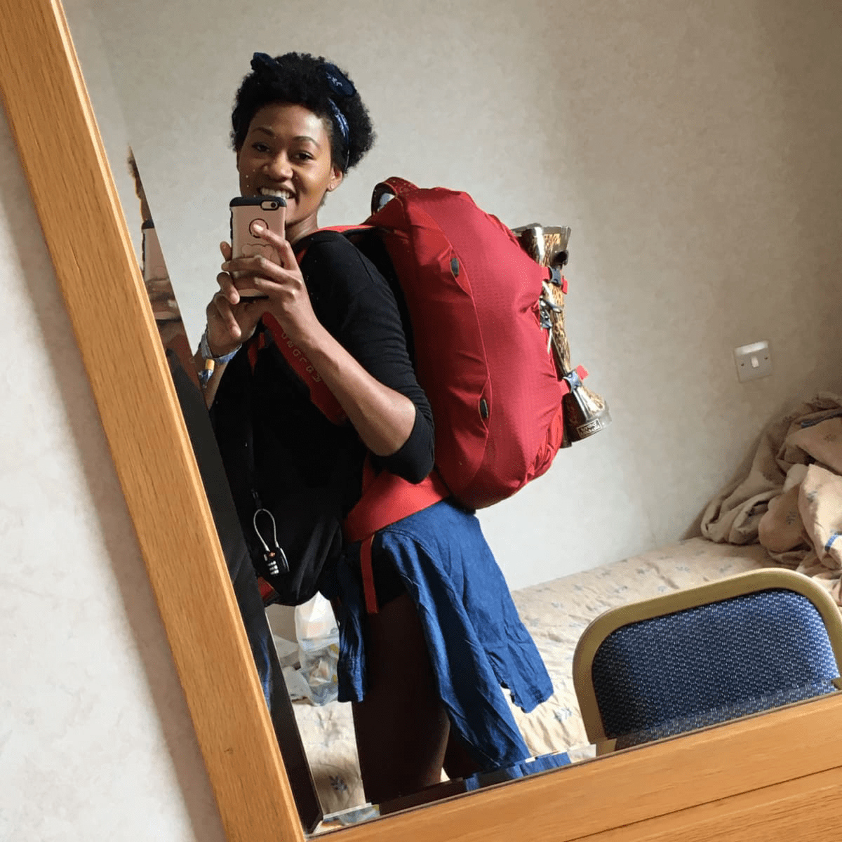 Black natural hair backpacker taking selfie in the mirror of a hotel room wearing a red Osprey backpack and a black bag Black natural hair backpacker taking selfie in the mirror of a hotel room wearing a red Osprey backpack and a black bag