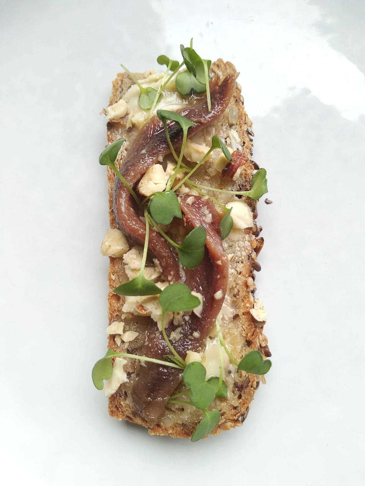 Tartine de pain au sarrasin, filets d'anchois, noisettes et micro-pousses de roquette Tartine de pain au sarrasin, filets d'anchois, noisettes et micro-pousses de roquette