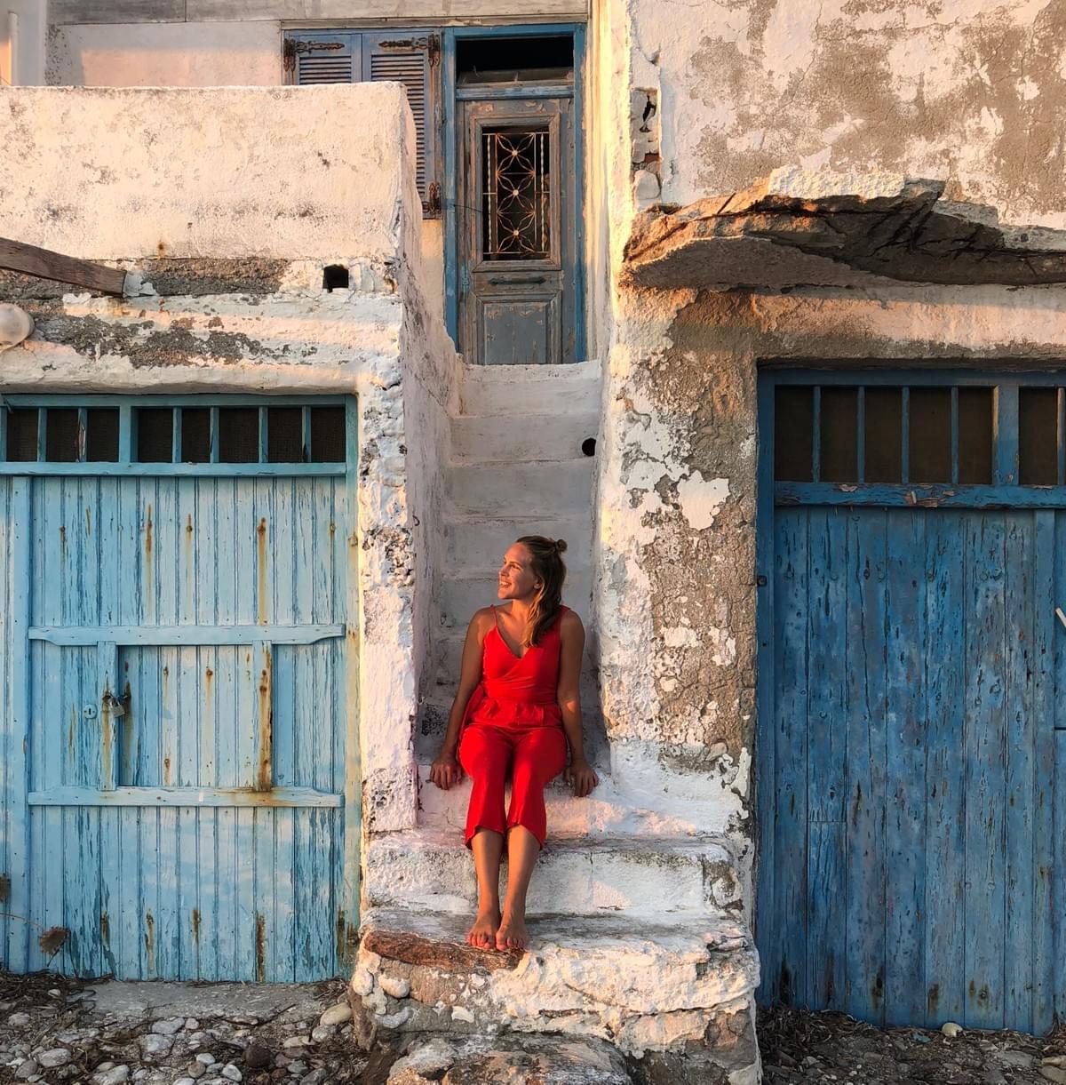 Woman smiles while sitting on stairs between two old buildings in Klima, Greece Woman smiles while sitting on stairs between two old buildings in Klima, Greece