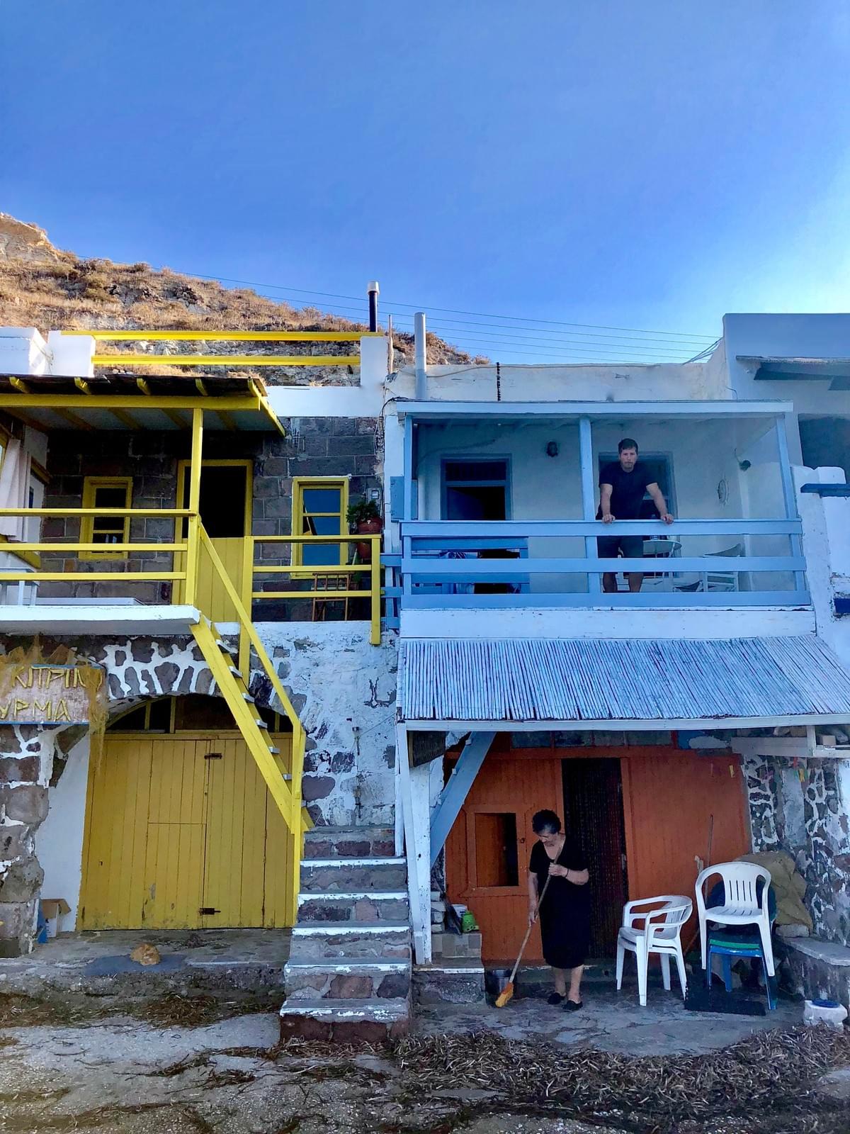 Man looks out of a balcony while an old woman sweeps the front of her house in Klima, Milos Man looks out of a balcony while an old woman sweeps the front of her house in Klima, Milos