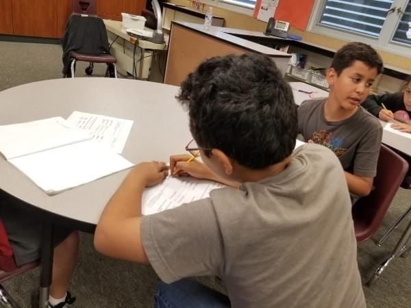 two boys at classroom table work together on worksheet two boys at classroom table work together on worksheet