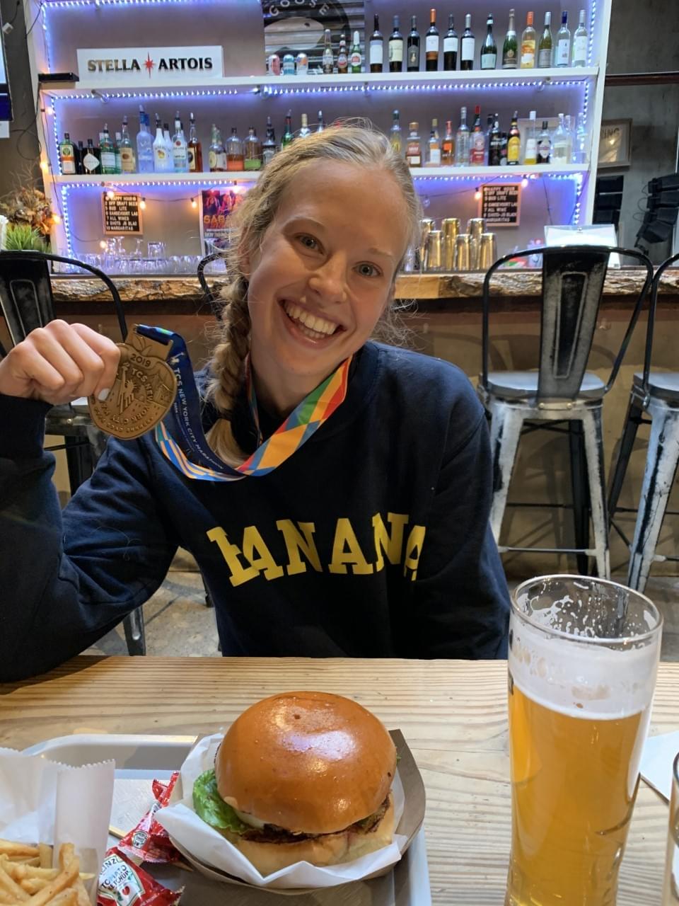 A New York marathon runner celebrates with her medal and a meal after completing the marathon A New York marathon runner celebrates with her medal and a meal after completing the marathon