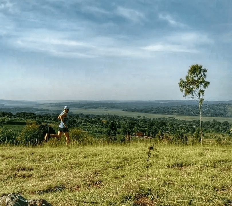 A Trail runner begins a descent from a ridge in Ndegeya, Uganda high above spectacular rural views in the background A Trail runner begins a descent from a ridge in Ndegeya, Uganda high above spectacular rural views in the background