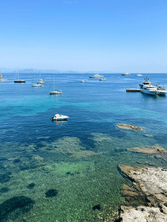 Boats anchored near rocky coastline in clear blue water