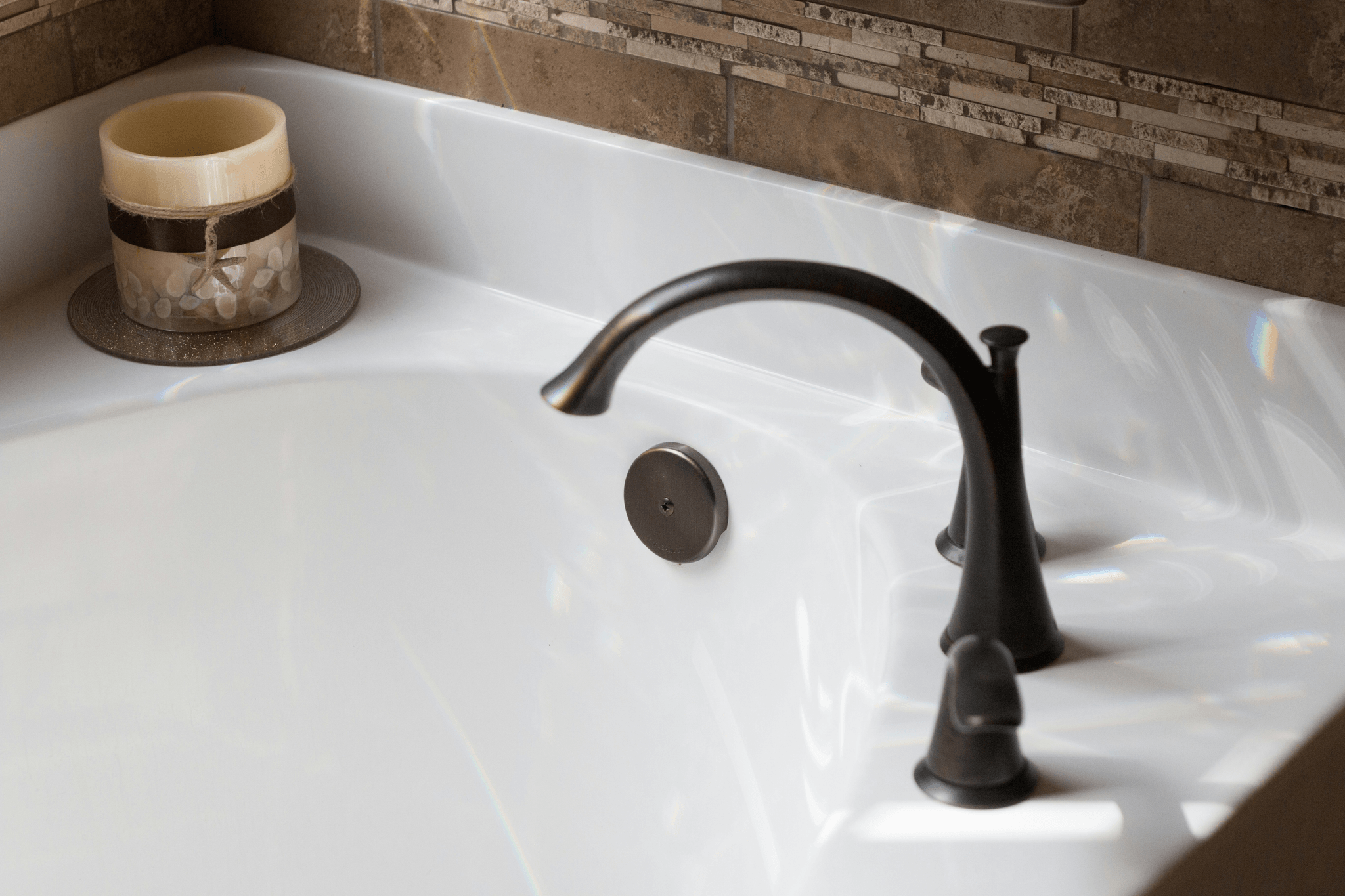 A white partial tub in photo with a brushed bronze faucet and a candle on the tub corner. 