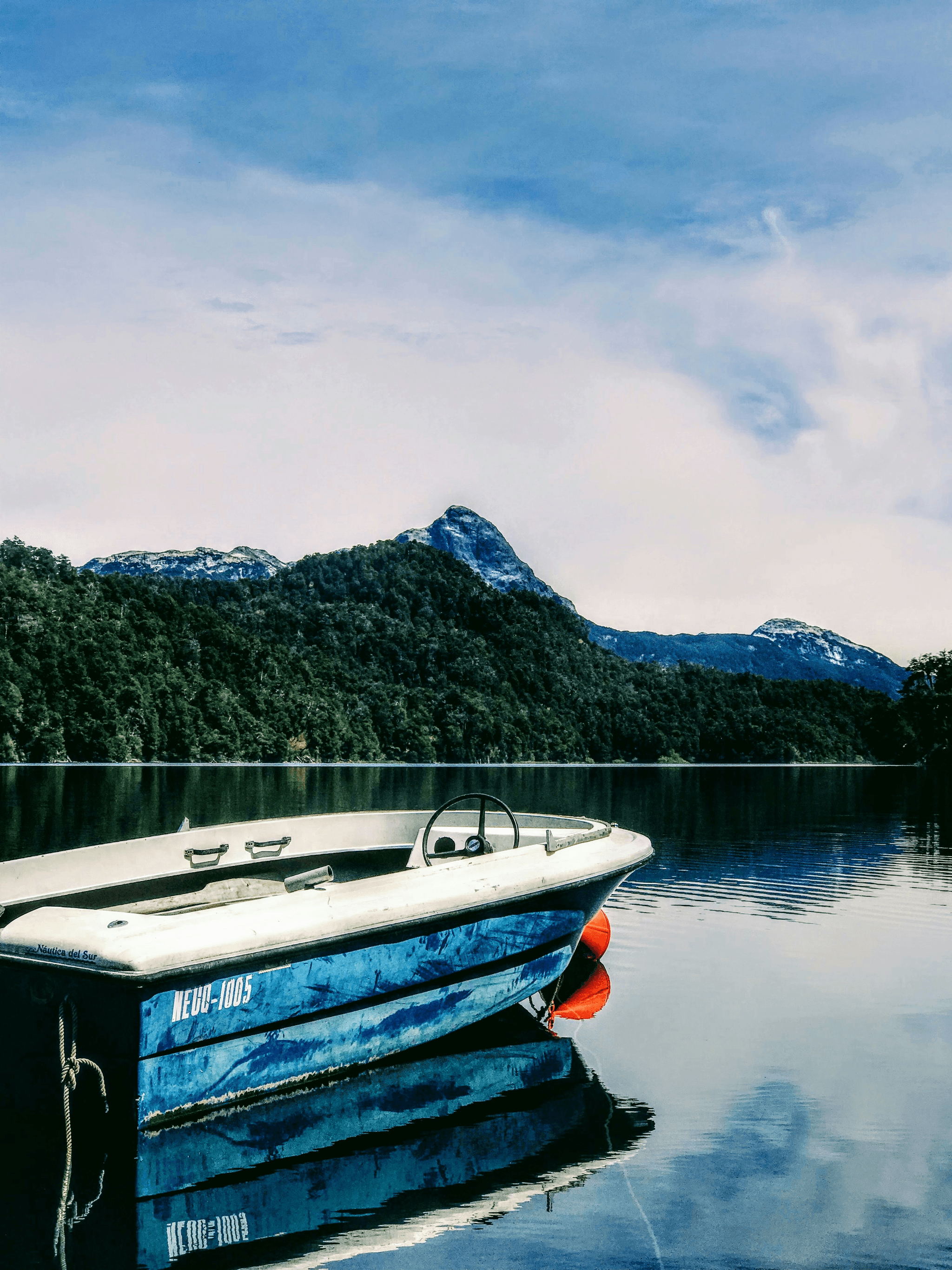 A small aluminum boat cruising on calm waters with mountains in background