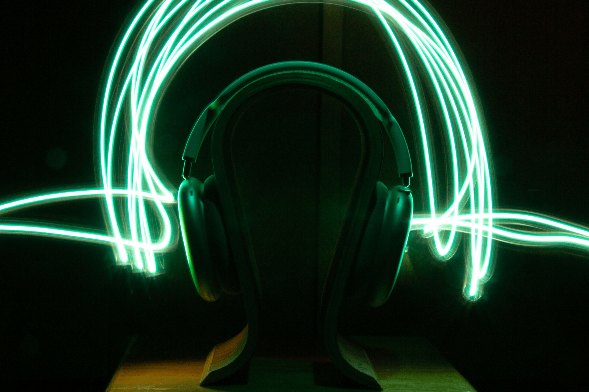 A pair of over‑ear headphones on a stand in a dark setting, surrounded by bright green looping light trails that create a sense of motion.