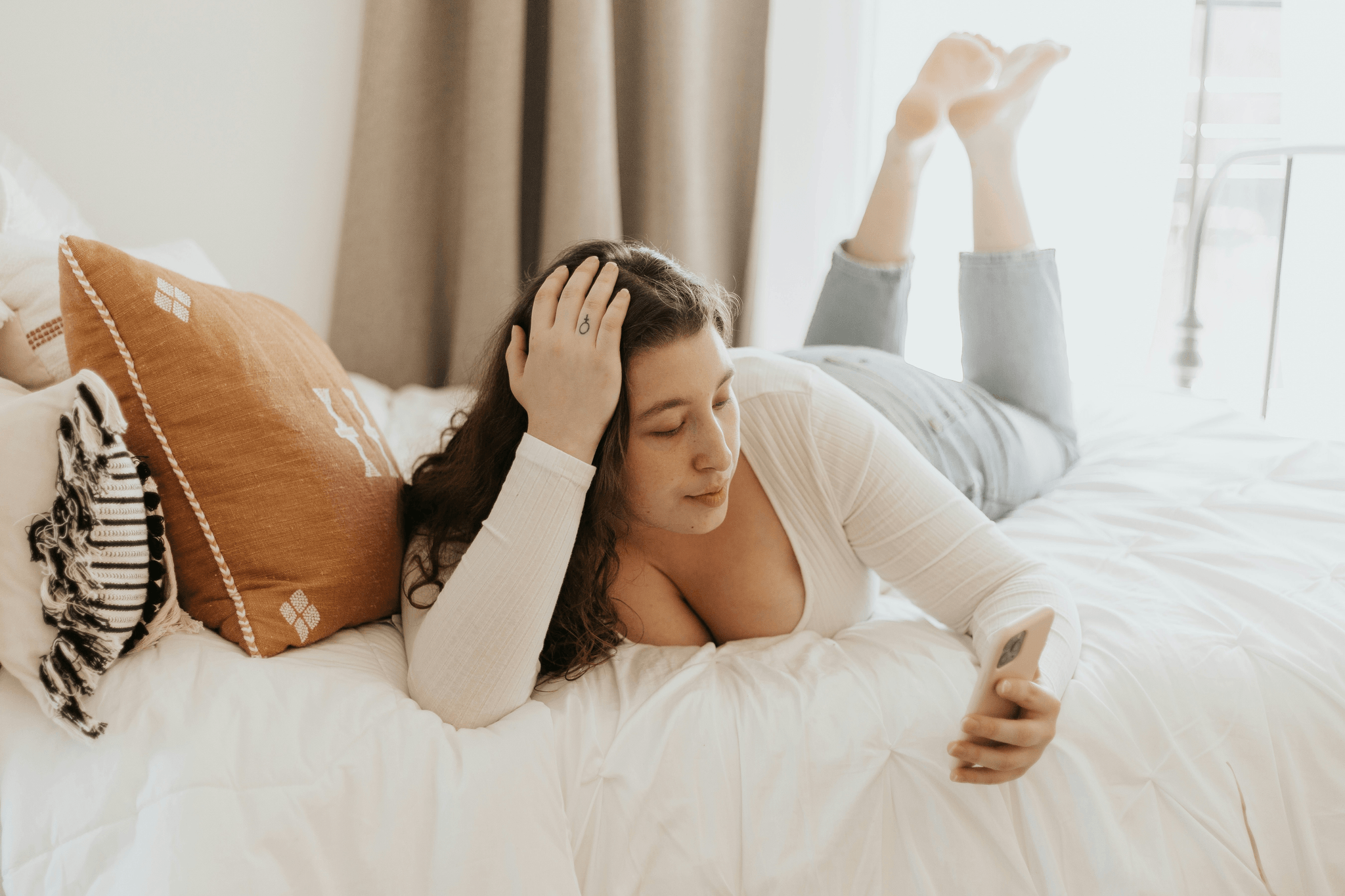 Woman lying on her bed on her phone to her therapist representing warm, approachable online therapy session in a safe space.