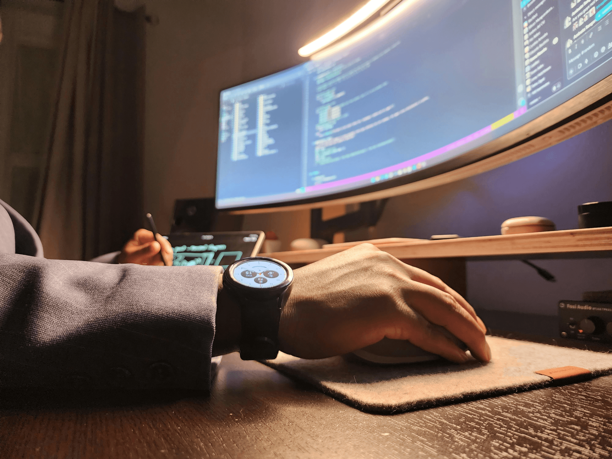Photo of a man with a large watch looking at a computer screen, while holding a mouse. 